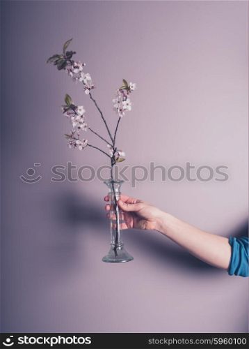 A female hand is holding a small vase with some pink flowers in it