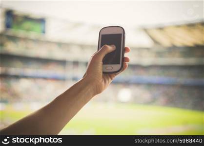 A female hand is holding a smart phone in a stadium to take pictures of a sporting event