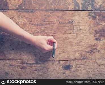 A female hand is writing on a wooden desk with a pen