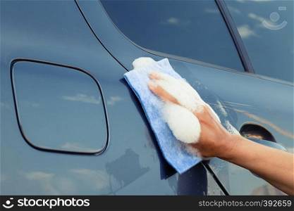 A female hand with a sponge in a soapy foam washes the car