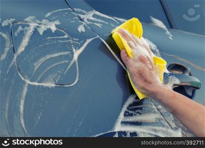 A female hand with a yellow sponge in a soapy foam washes the car. Female hand with yellow sponge in soapy foam washes the car