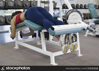 A female lies on a hamstring curl machine in a gym