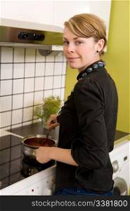 A female looking at the camera and smiling while cooking at home in her apartment.