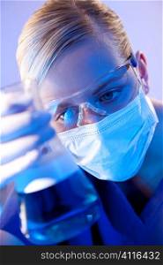 A female medical or scientific researcher or doctor looking at a flask of red liquid in a laboratory.