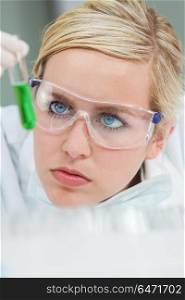 A female medical or scientific researcher or doctor looking at a green solution in a laboratory . Female Scientist & Green Test Tube In Laboratory