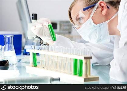 A female medical or scientific researcher or doctor looking at a test tube of green solution in a laboratory.