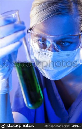 A female medical or scientific researcher or doctor looking at a test tube of green solution in a laboratory