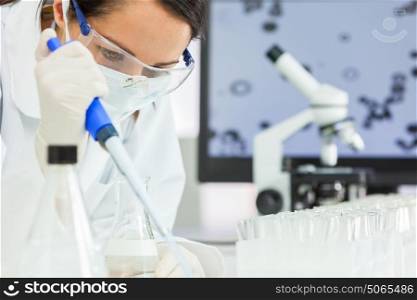 A female medical or scientific researcher or scientist using a pipette, flask and microscope in a laboratory