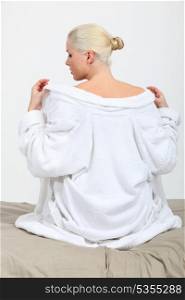 A female model taking her bathrobe off on her bed.