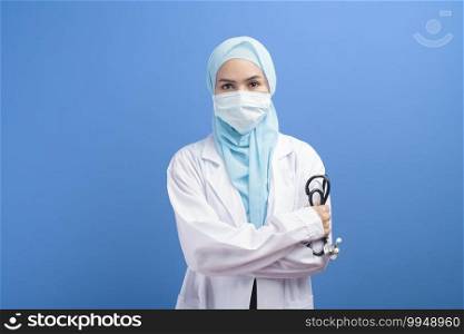 A female muslim doctor with hijab wearing a surgical mask over blue background studio.. Female muslim doctor with hijab wearing a surgical mask over blue background studio.