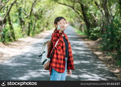 A female tourist carrying a backpack and raising her five fingers to ban on the road