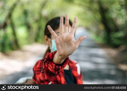 A female tourist carrying a backpack and raising her five fingers to ban on the road