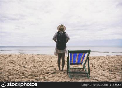A female traveler with hat and backpack standing alone on the beach by the sea