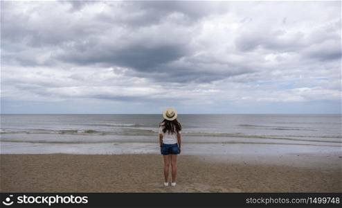 A female traveler with hat standing alone on the beach by the sea