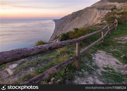 A fence of tree trunks on the edge of a cliff on a rocky sea coast