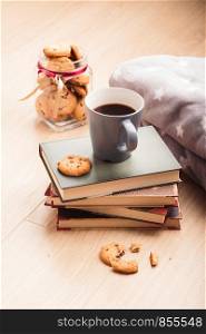 A few books with cup of coffee and cookies on wooden floor