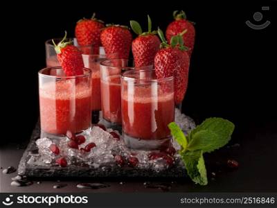 a few glasses of drink with strawberry and ice on a black stone on a dark background. beverages on a dark background