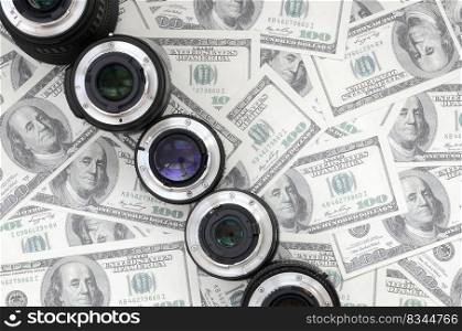 A few photographic lenses lies on the background of a lot of dollar bills. Space for text
