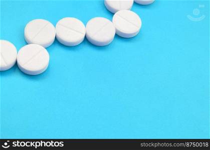A few white tablets lie on a bright blue background surface. Background image on medical and pharmaceutical topics