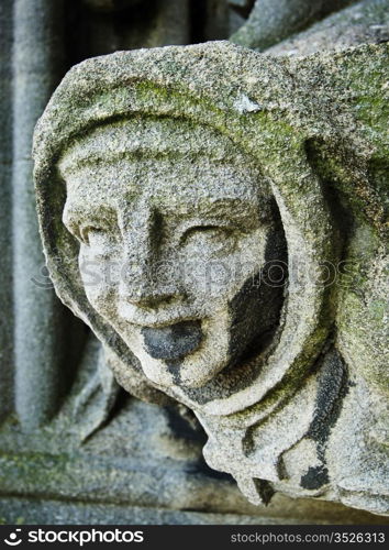 A figure of a weathered gargoyle on the belltower of the Church of St. Mary The Virgin in Oxford, England. The carving appears to be a monk in a robe and cowl.