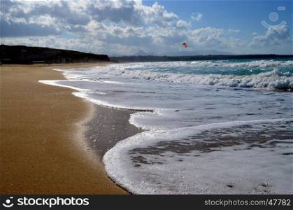 A fine sand beach with a hill, a blue sky and waves.