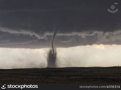 A fine tornado dances within a cloud of dust that moves in ringlets up the lower half of the tornado