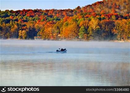 A fishing boat going across the lake in the early autumn morning fog.