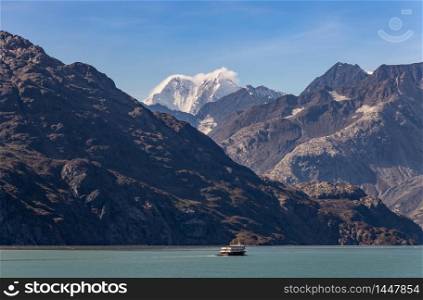 A fishing boat sailing in Alaska with huge mountains and snowy peak in the background