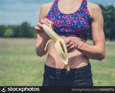 A fit and athletic young woman is peeling a banana in the park on a sunny summer day