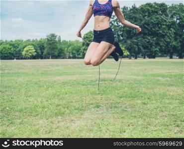 A fit and athletic young woman is skipping with a jump rope in the park on a summer day