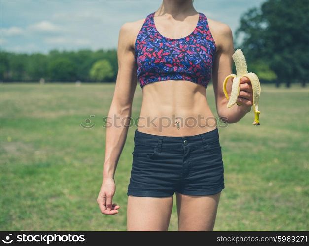 A fit and athletic young woman is standing in a park with a banana