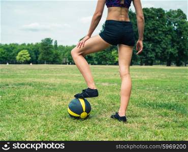 A fit and athletic young woman is standing on the grass in a park with a medicine ball
