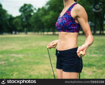 A fit and athletic young woman is standing on the grass in a park with a jump rope