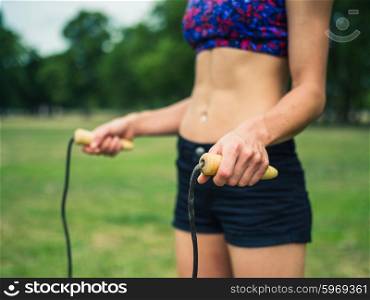 A fit and athletic young woman is standing on the grass in a park with a jump rope