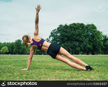 A fit and athletic young woman is working out in a park and is doing a half angel exercise on the grass