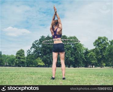 A fit and athletic young woman is working out with a hula hoop in the park on a sunny summer day