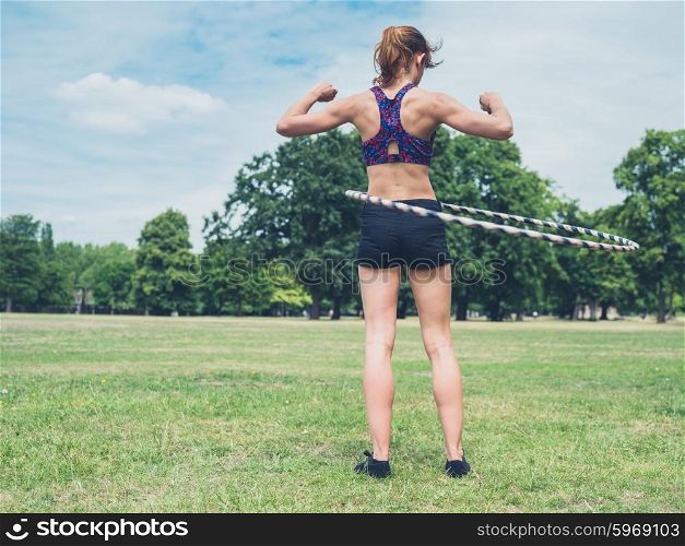 A fit and athletic young woman is working out with a hula hoop in the park on a sunny summer day