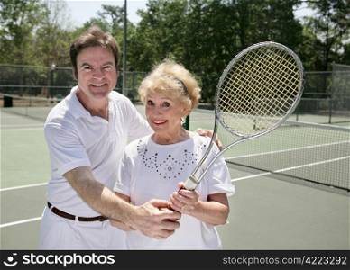 A fit senior lady getting a tennis lesson from a handsome young pro.