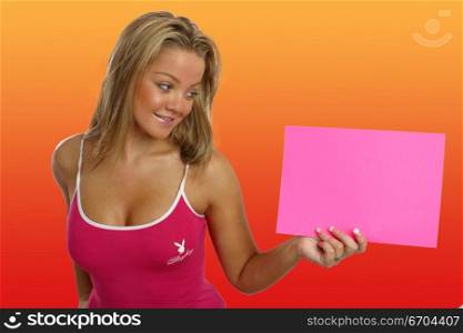 A fit young girl glamorously poses in the studio holding a card for text insertion.