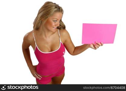 A fit young girl glamorously poses in the studio holding a card for text insertion.
