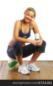 A fit young girl glamorously poses in the studio wearing sports wear and sitting on a basketball.