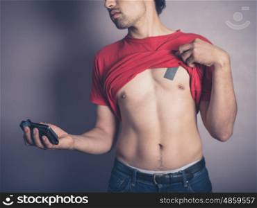 A fit young man is lifting up his shirt to take a selfie of his toned body