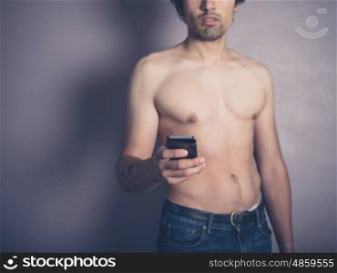 A fit young shirtless man is using a smartphone