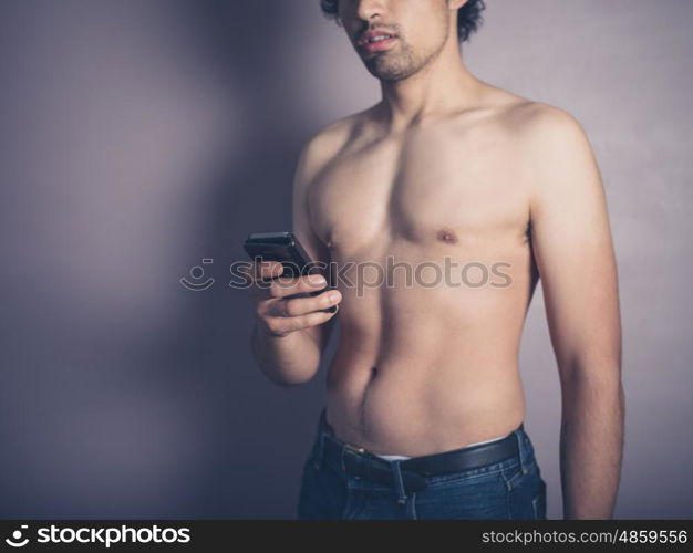 A fit young shirtless man is using a smartphone