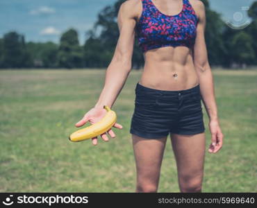 A fit young woman is standing in a park and is offering a banana