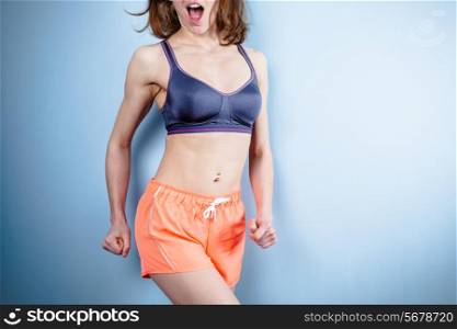 A fit young woman with a toned stomach in sports bra and workout shorts is smiling