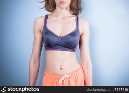 A fit young woman with a toned stomach is wearing a sports bra and workout shorts