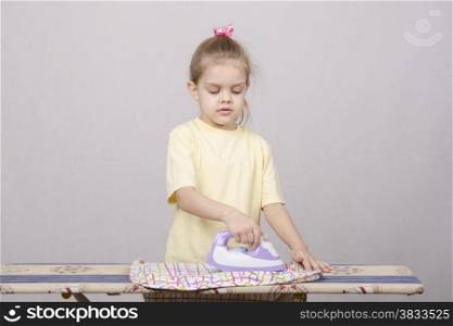 A five year old girl playing in a housewife, and stroking things iron