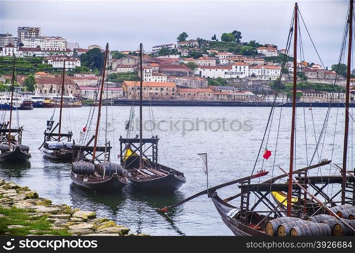 A fleet of boats are lined up against the banks of the Douro River in Porto, Portugal. Historically, these boats transported the barrels, or pipes, of port wine from the vineyards to the wineries in the city of Porto.