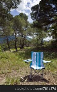 A foldable camping chair surrounded by trees depicting summer vacation